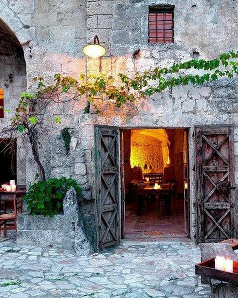 A candlelit stone courtyard with an arched recess and open timber doors &mdash; Sextantio Le Grotte della Civita, Matera, Italy