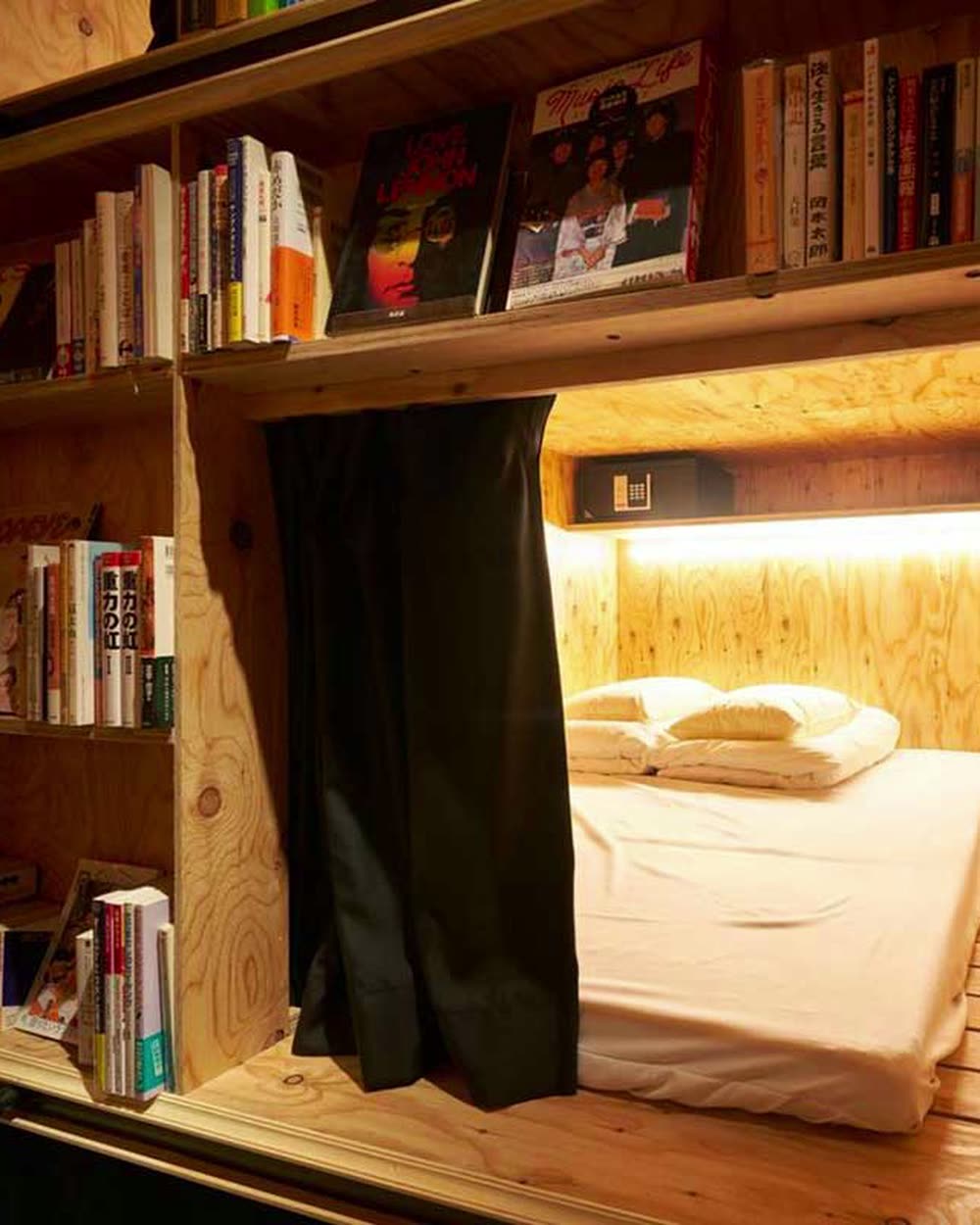A sleeping berth built into bookshelves, spines beside the pillow &mdash; Book and Bed Tokyo, Tokyo, Japan