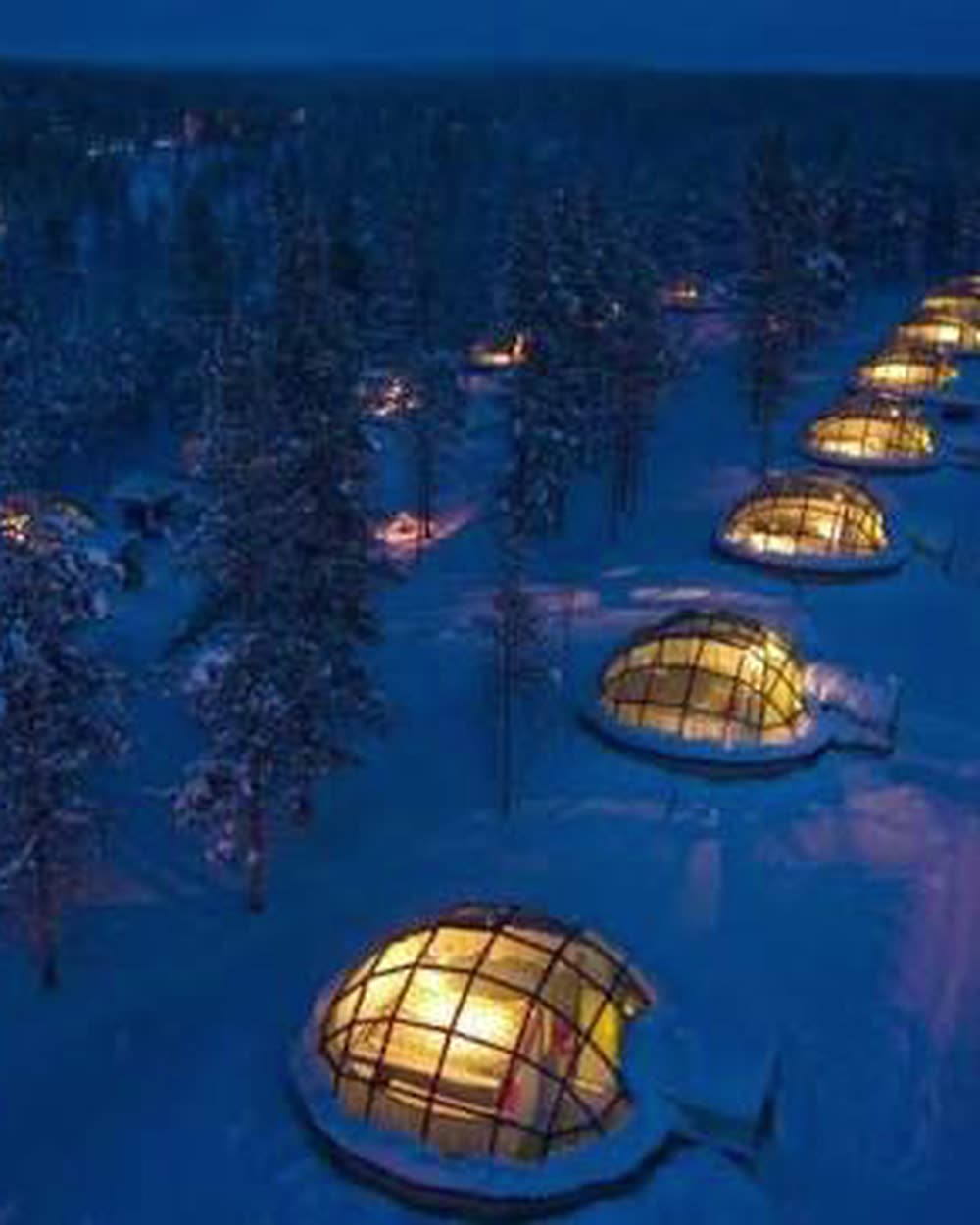 Glass domes lit from within among snow-covered trees at night &mdash; Kakslauttanen Arctic Resort, Saariselkä, Finland