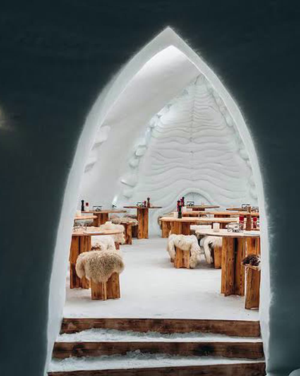 A snow arch opening onto a lit dining room with wooden tables &mdash; Iglu-Dorf Davos-Klosters, Davos, Switzerland